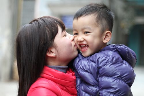 Free A joyful moment of a mother kissing her smiling son outdoors in winter clothing. Stock Photo