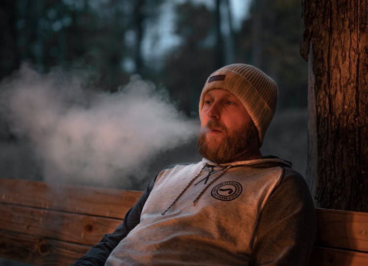 Man Sitting On A Bench Blowing Out Smoke