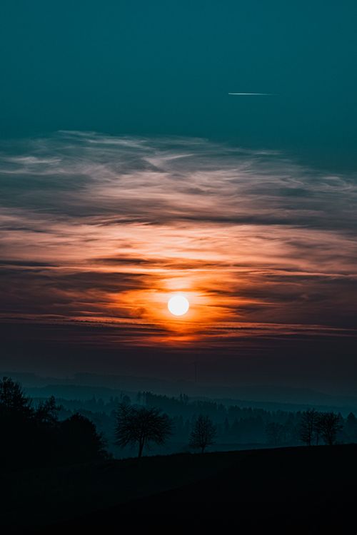 Free A stunning sunset scene with silhouetted trees and vibrant cloud patterns in the sky. Stock Photo