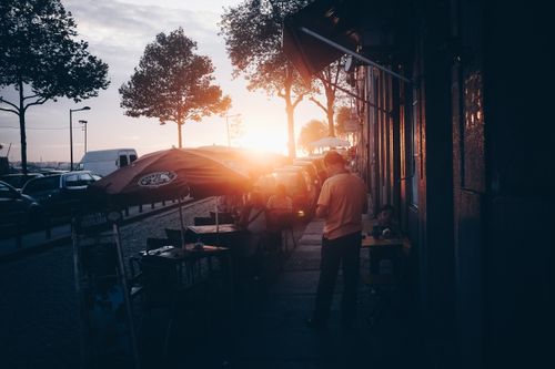 Free People silhouetted against a vibrant sunset in an urban street scene with trees and vehicles. Stock Photo