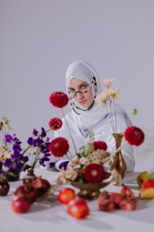 Woman in White Dress and Headscarf Sitting at a Table Decorated with Flowers