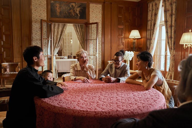 Multiracial Family Sitting At Table And Talking With Smile On Faces