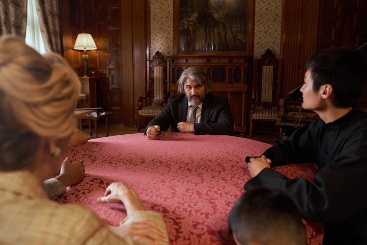 Family At Table Listening To Head Of Family Sitting On Opposite Side