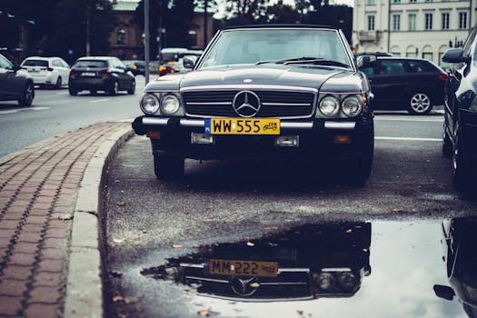 A classic Mercedes-Benz with a reflection in a puddle on an urban street.