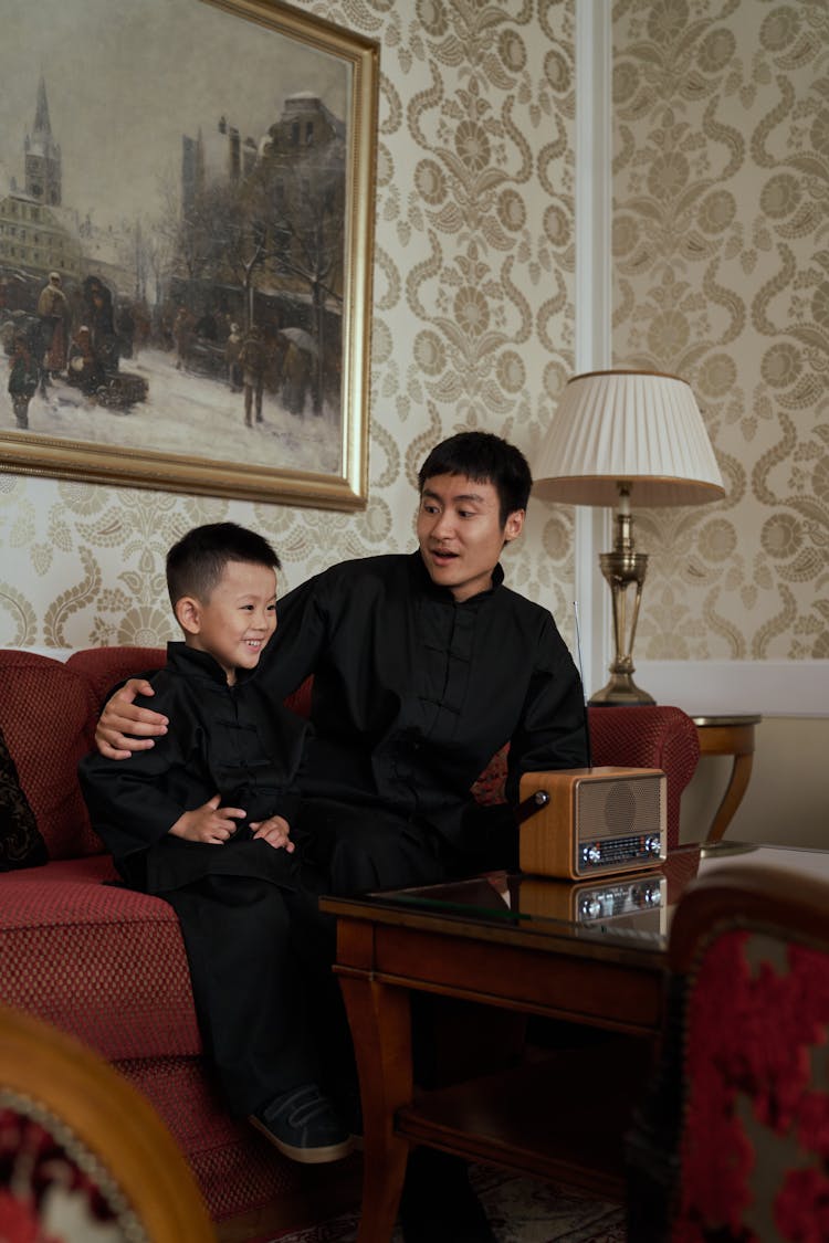 Father And Son In Traditional Chinese Outfits Sitting On Sofa And Talking