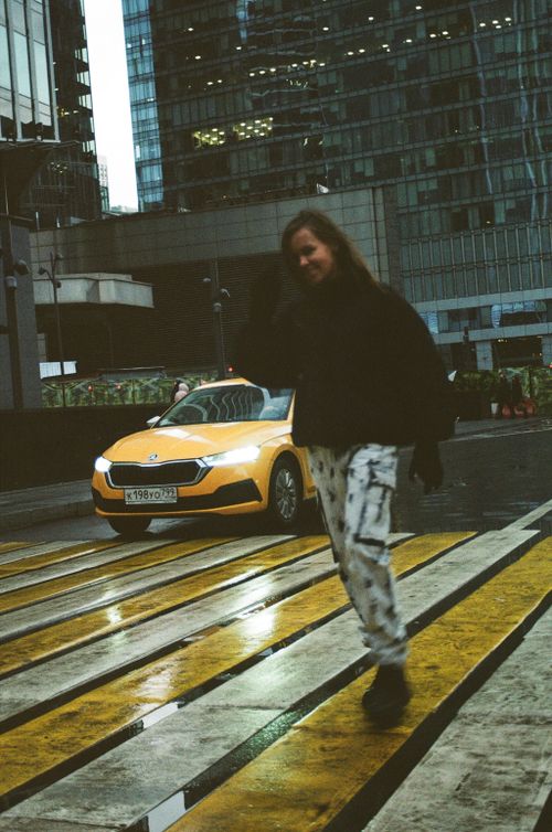 Free Woman crossing a city street, captured in an urban environment with a yellow taxi in the background. Stock Photo