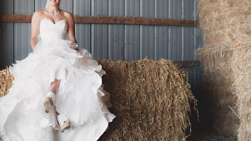 Женщина в белом свадебном платье без бретелек с вырезом сердечком сидит на коричневом сене