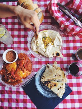 Top view of Israeli meze including hummus and pita on a red checked tablecloth.