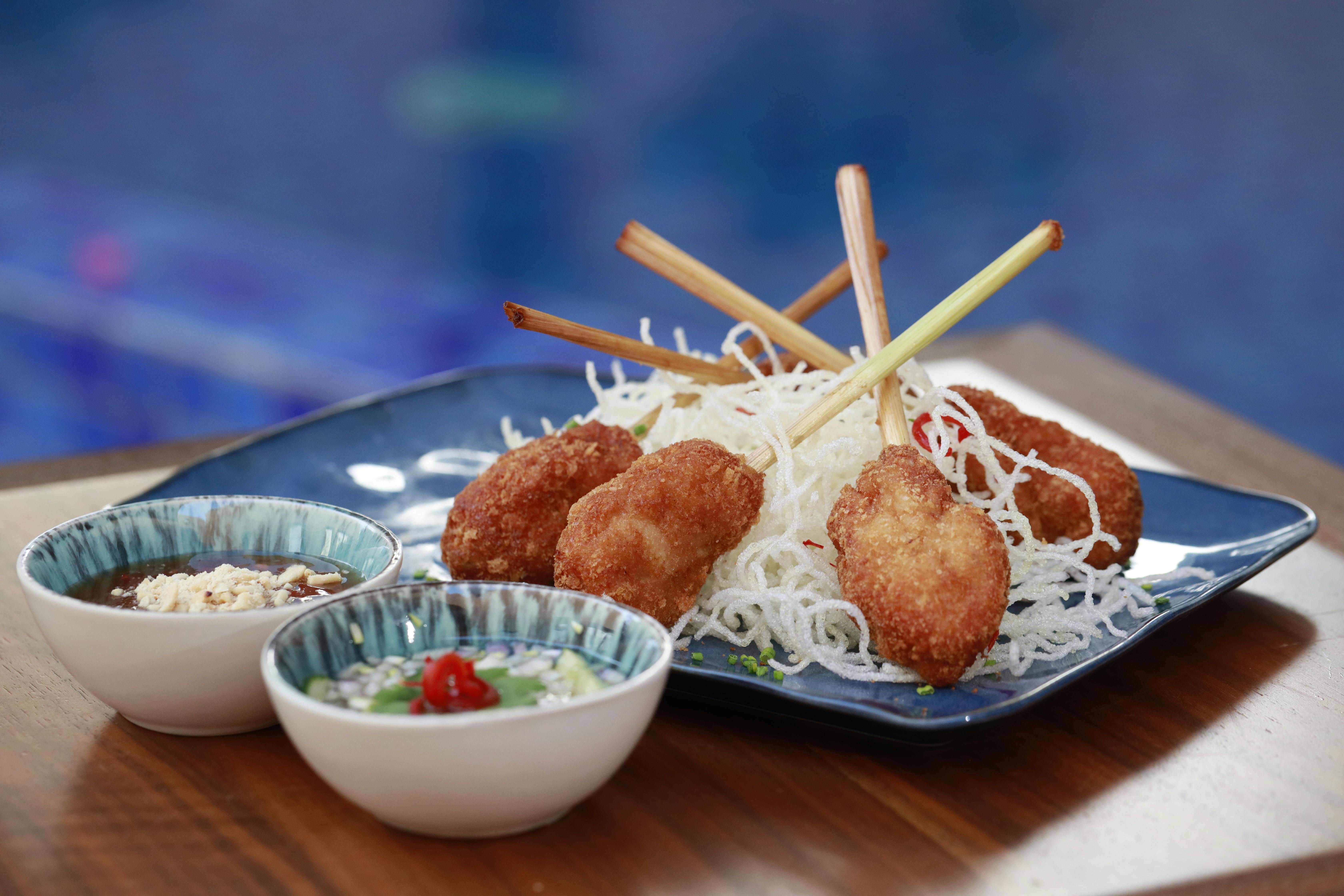 Delicious Asian-style skewers garnished with crispy noodles and served with dipping sauces on a wooden table.