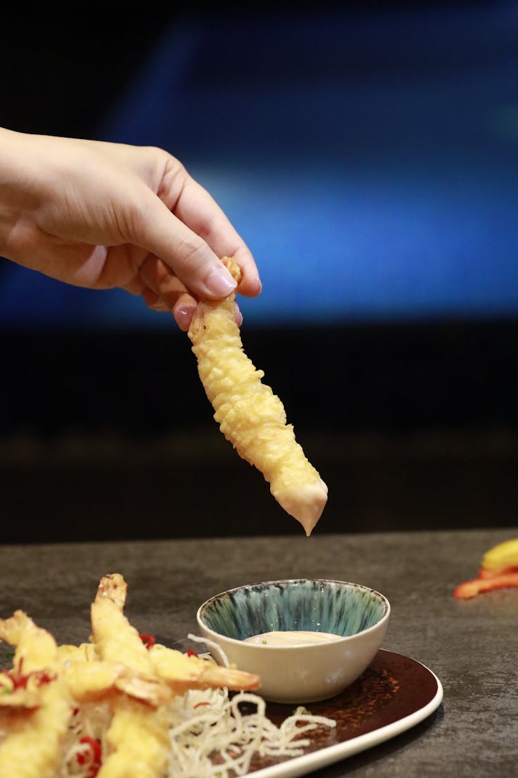 A Hand Holding A Tempura With Sauce