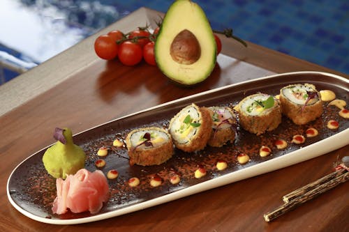 A Tray of Sushi Near a Sliced Avocado on a Wooden Table