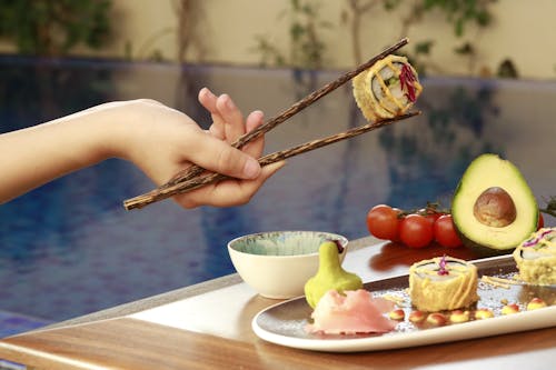 A Person Holding a Sushi Roll with a Chopstick