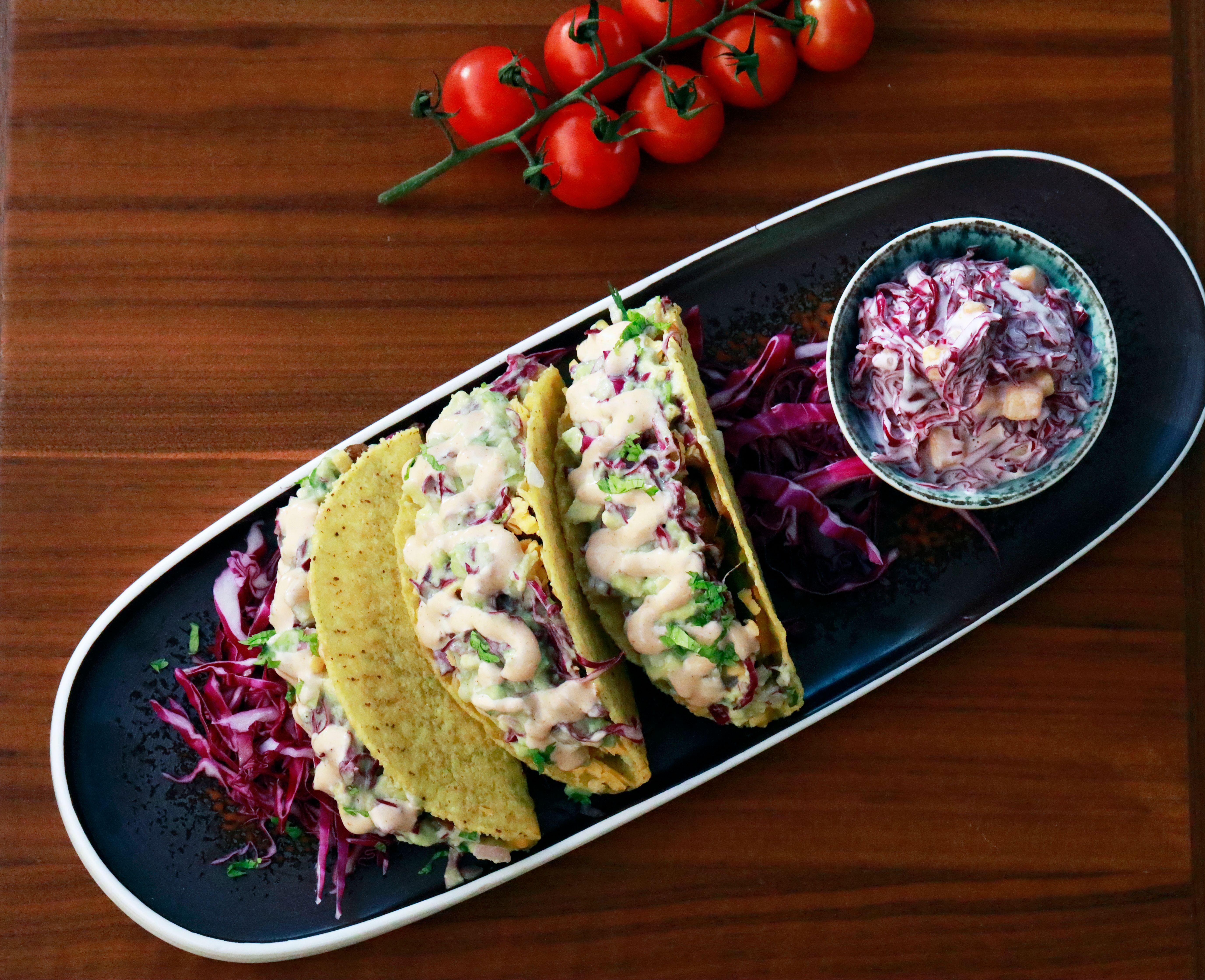Top view of fish tacos with creamy sauce and red cabbage salad on a wooden table.