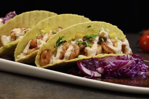 Free Close-up of shrimp tacos with creamy sauce and fresh vegetables on a plate, perfect for food photography. Stock Photo