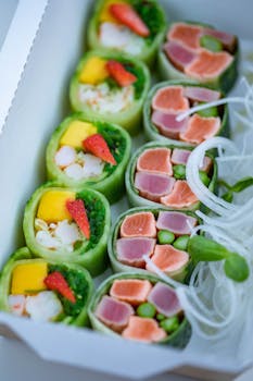 Colorful sushi rolls with salmon, tuna, and fresh fruits in a box, ready to serve.