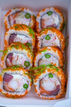 Vibrant sushi rolls with roe, surimi, and rich ingredients in takeout box.
