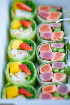 An assortment of vibrant sushi rolls featuring salmon, tuna, mango, and strawberries in a tray.