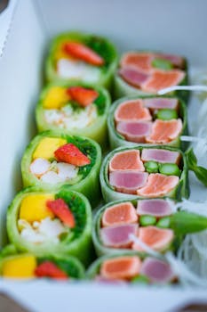Colorful sushi rolls with fresh tuna, salmon, and fruits in a takeout box.