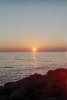 Tranquil view of the sunset over the sea from İstanbul's rocky shore, capturing beautiful colors and calm waters.