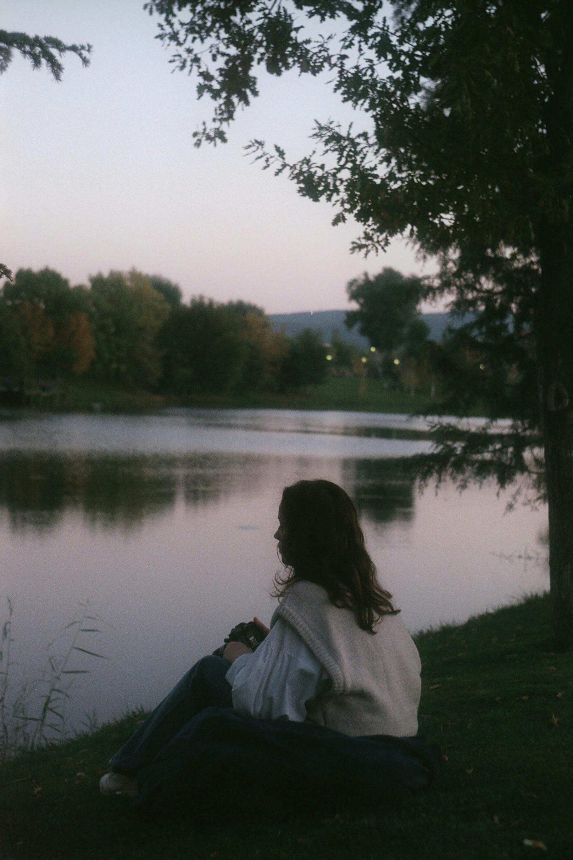 A woman sits peacefully by a lake in Eskişehir, Turkey, under the twilight sky.