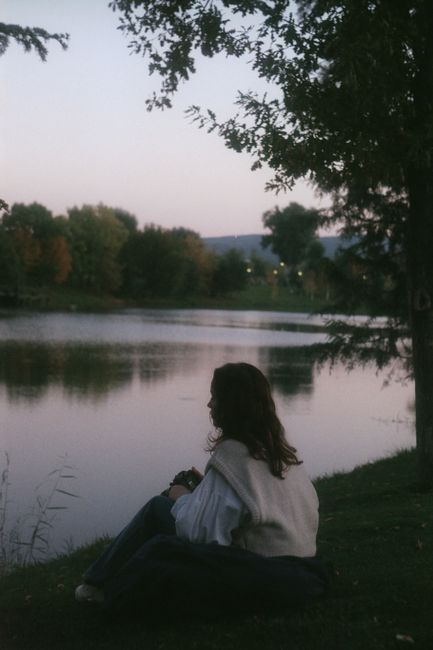 A woman sits peacefully by a lake in Eski艧ehir, Turkey, under the twilight sky.