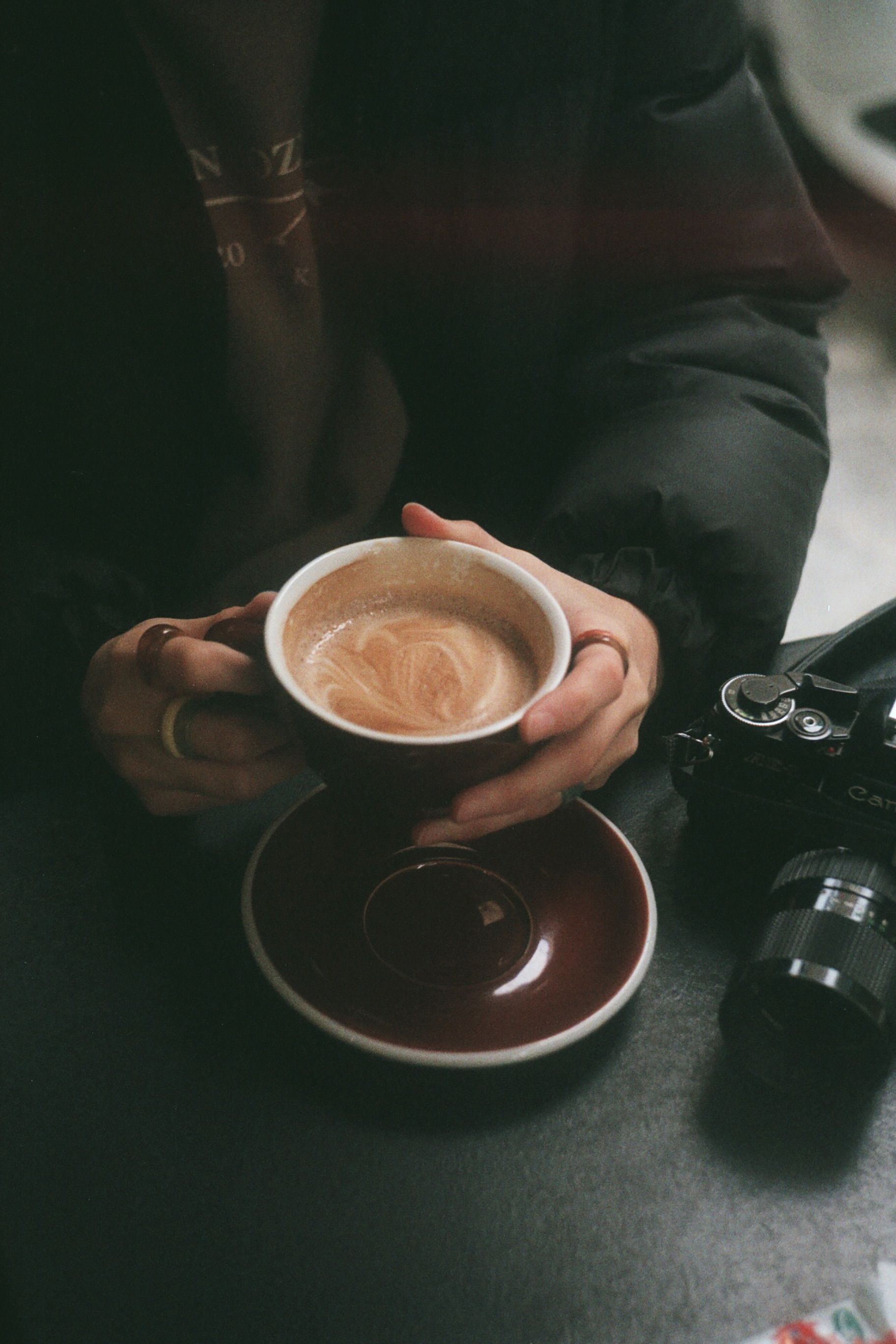 Warm coffee cup held by hands next to a vintage camera in an Istanbul café.