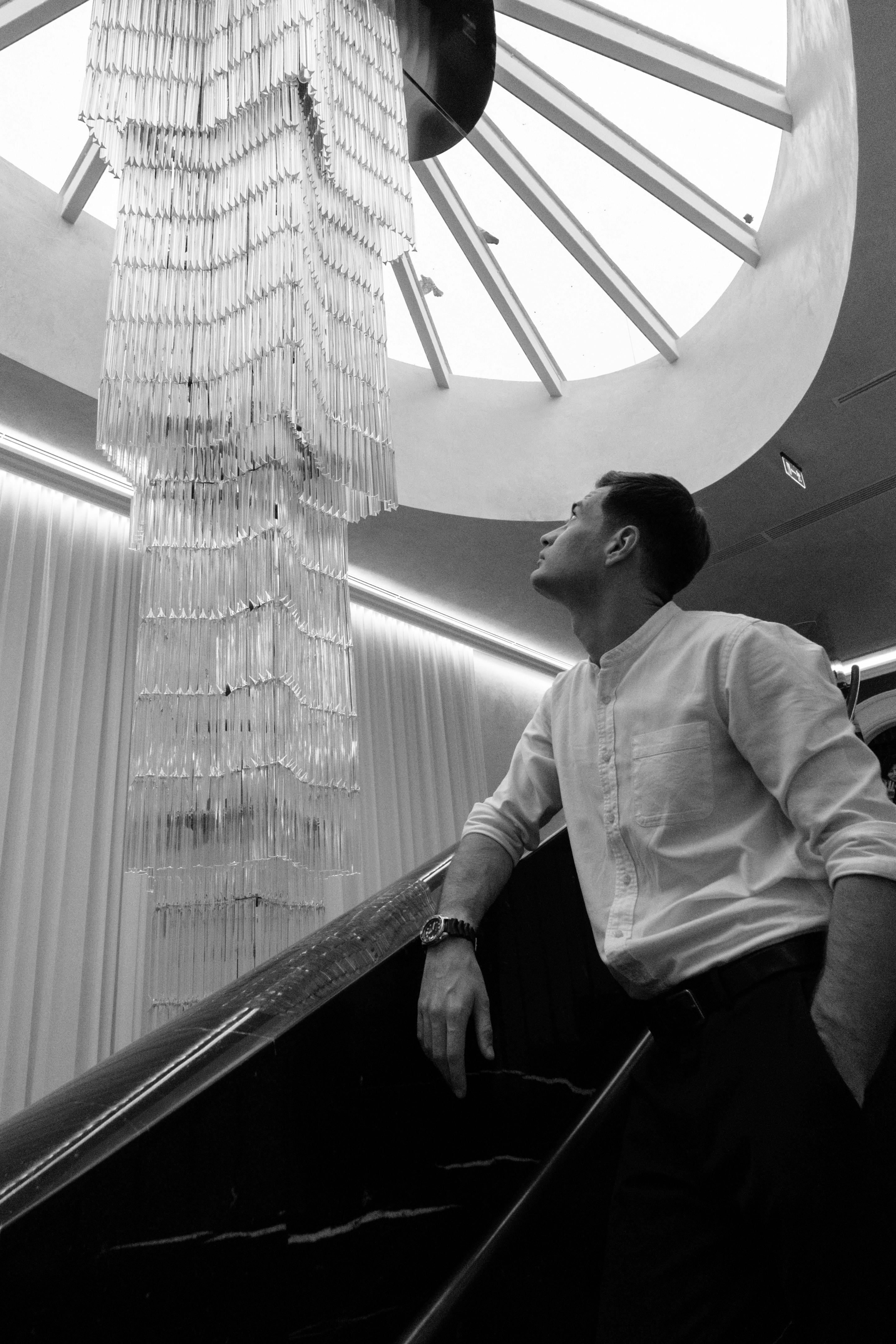 A man admiring an elegant chandelier in a monochrome indoor setting.