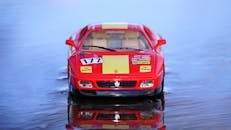 一辆引人注目的红色法拉利模型玩具车在反光水面上被拍摄，展现了其设计