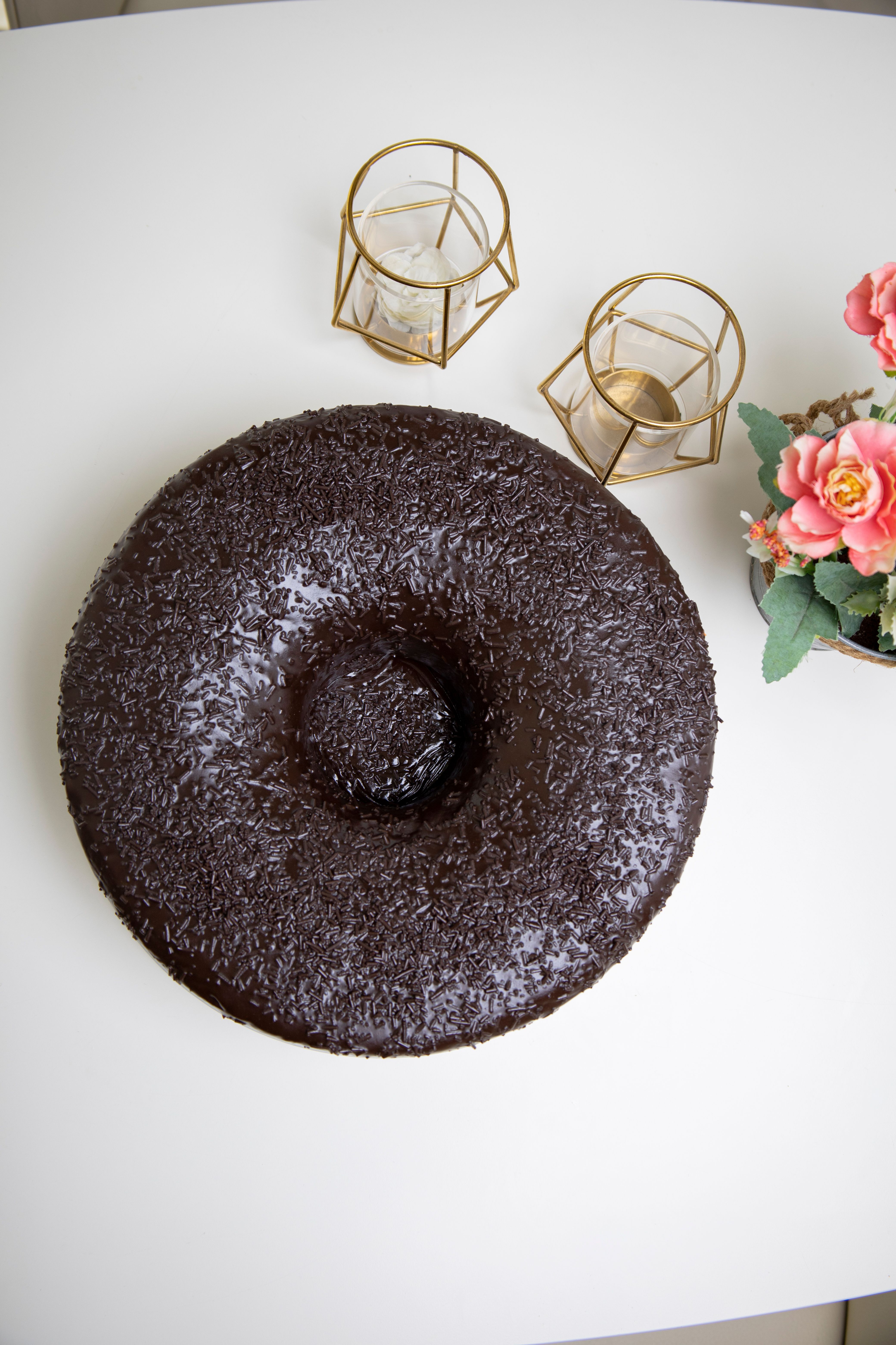 A mouthwatering chocolate cake on a white table with elegant candle holders and pink flowers.
