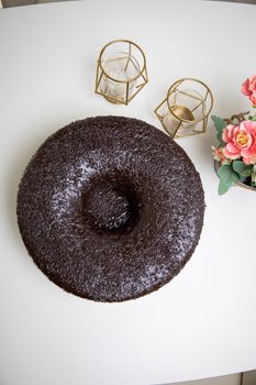A mouthwatering chocolate cake on a white table with elegant candle holders and pink flowers.
