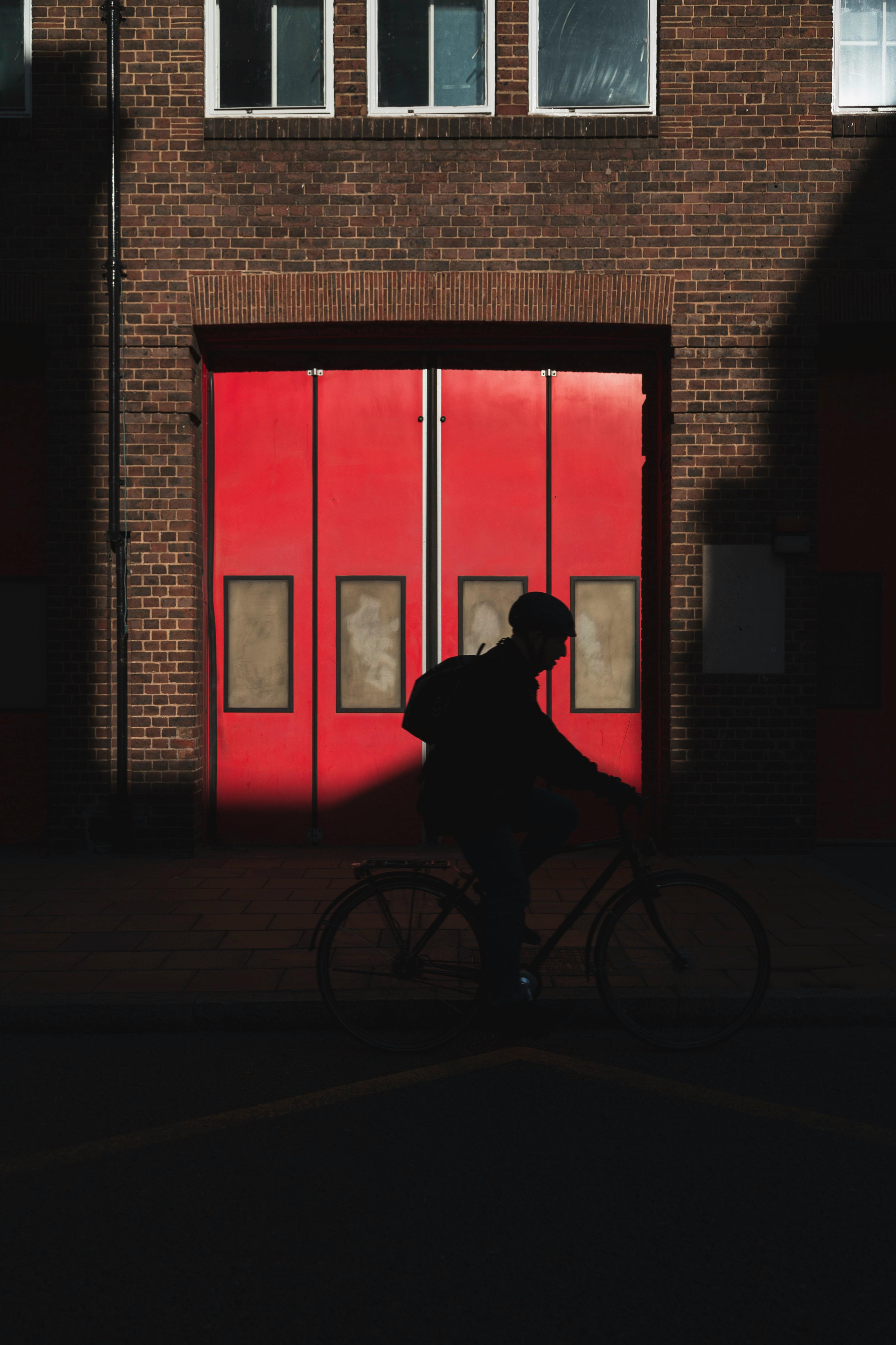 Silhouette of a person cycling past a vibrant red door set in a brick wall, capturing urban evening atmosphere.