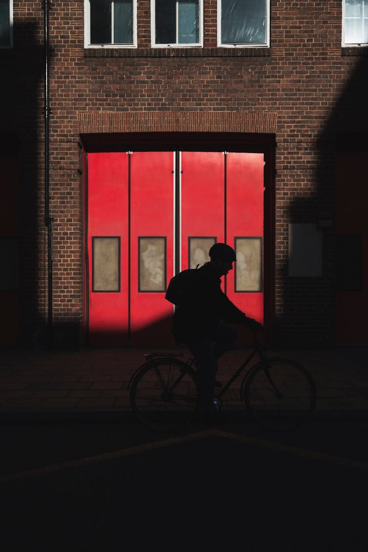 Silhouette Of Cyclist Riding In Street Along Building