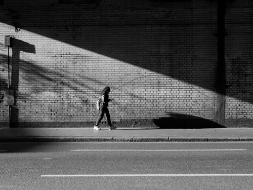 Free A person walks along an urban sidewalk, casting a shadow on a brick wall in a dramatic black and white scene. Stock Photo