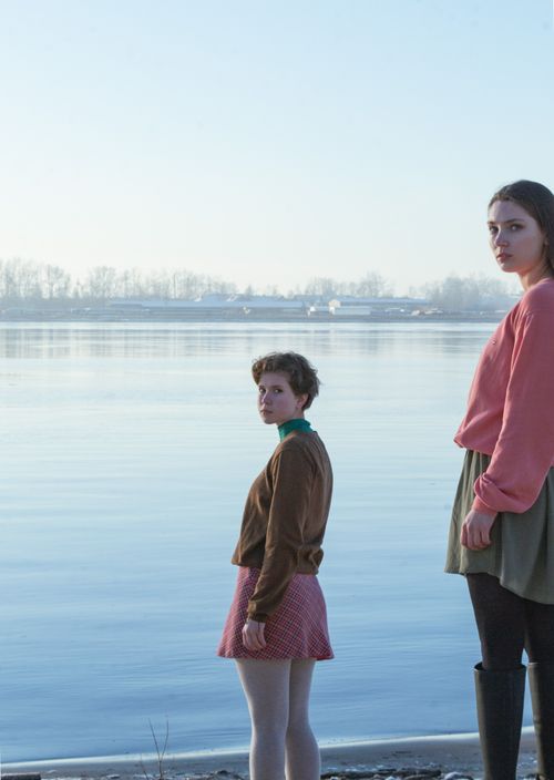 Free Two young women standing by a serene lake shore on a clear day. Stock Photo
