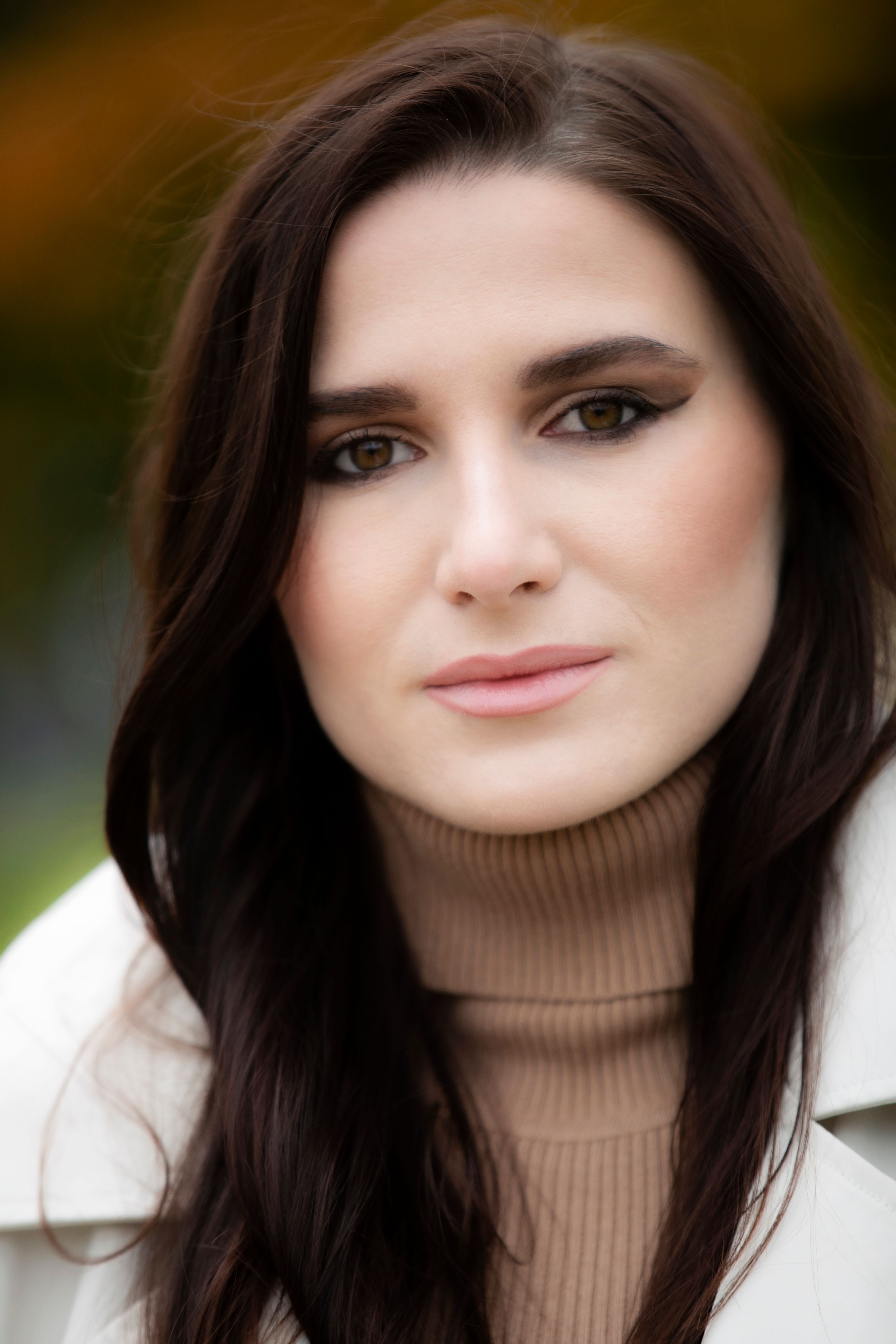 Close-up portrait of a brunette woman wearing a turtleneck sweater and coat. Soft blurred background.