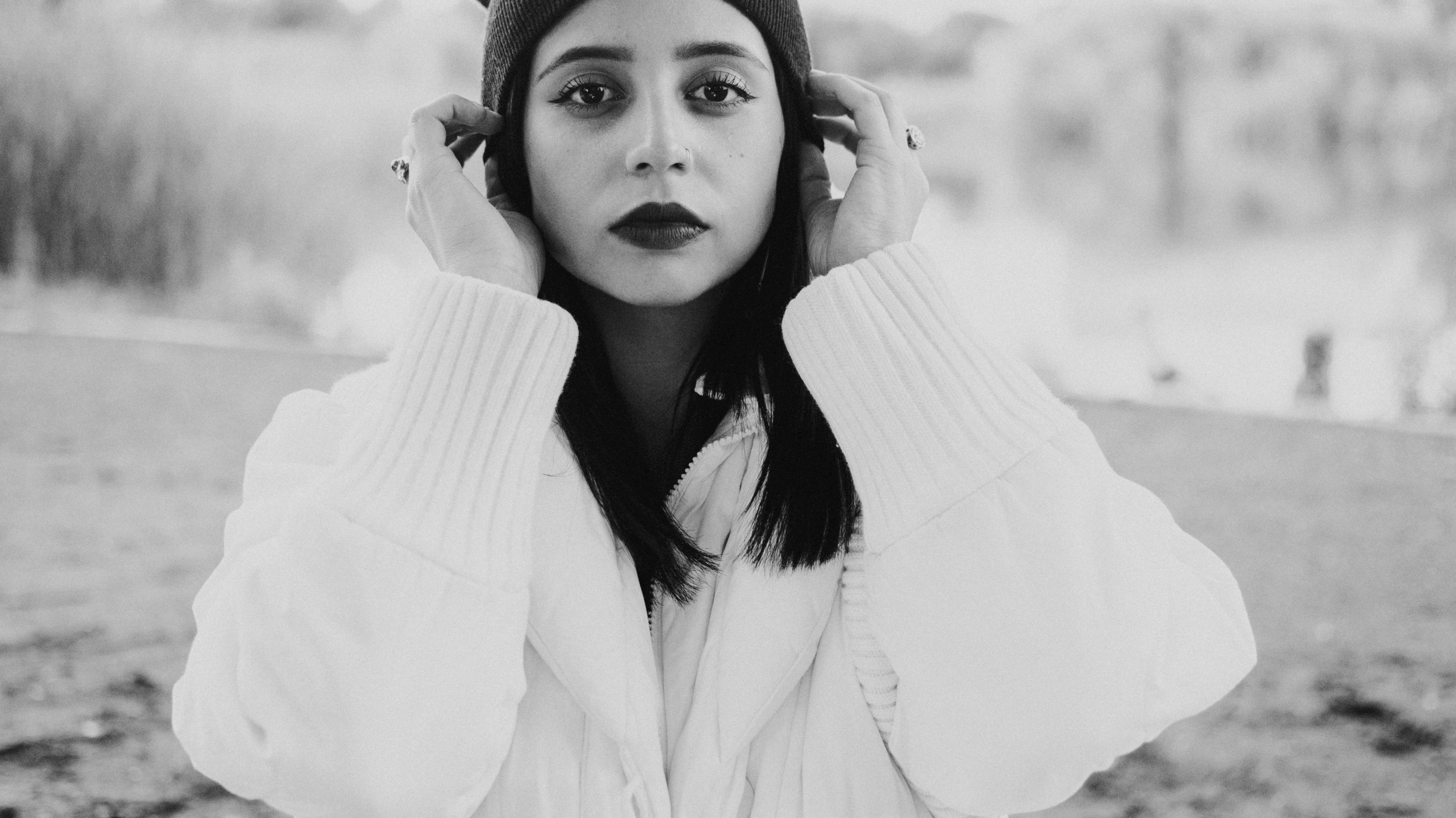 A striking black and white portrait of a young woman in a sweater and beanie, standing outdoors.