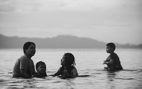 Grayscale Photo of Mother and Her Children Swimming on the Beach