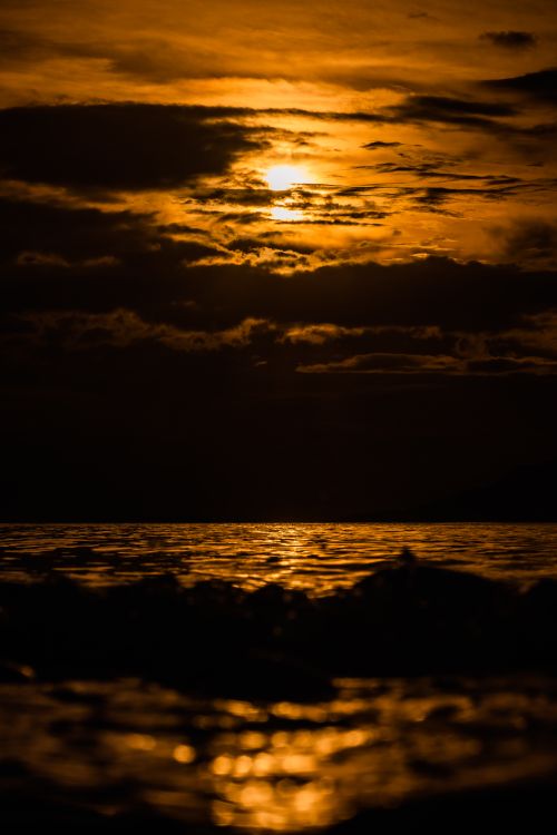 Free A captivating sunset over the ocean with dramatic clouds creating a warm, moody atmosphere. Stock Photo