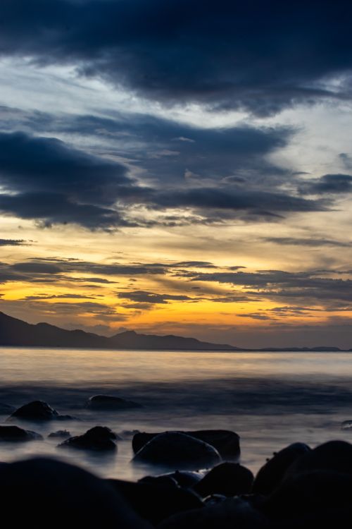 Free Peaceful sunset over rocky coastline with dramatic cloud formations and a tranquil sea. Stock Photo