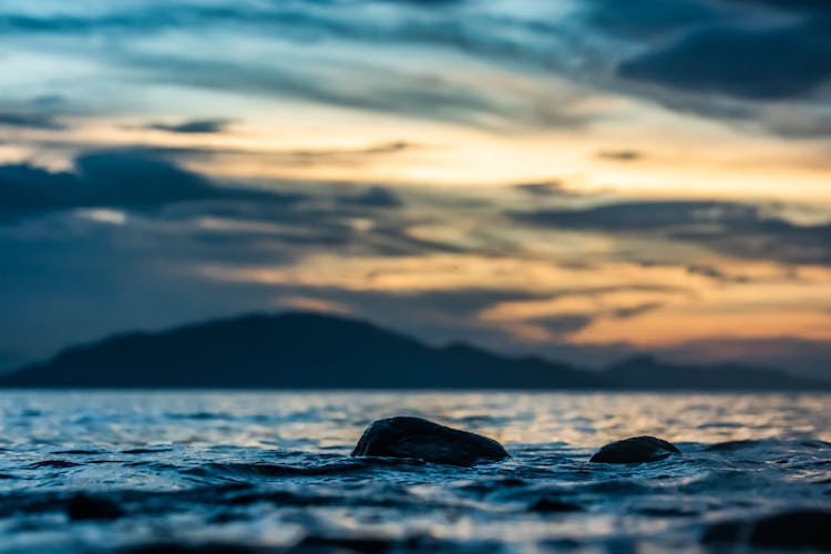 Rocks In Water And Island At Dusk