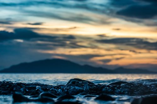 Free Vibrant sunset over a calm sea with rocky shoreline and dramatic clouds. Stock Photo