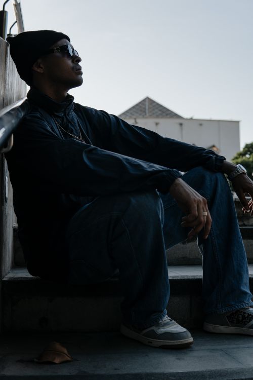 Free Man in urban streetwear sitting on concrete steps, wearing sunglasses and knit hat. Stock Photo