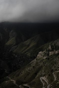 A dramatic aerial shot of rugged mountains under dense clouds, showcasing natural beauty.