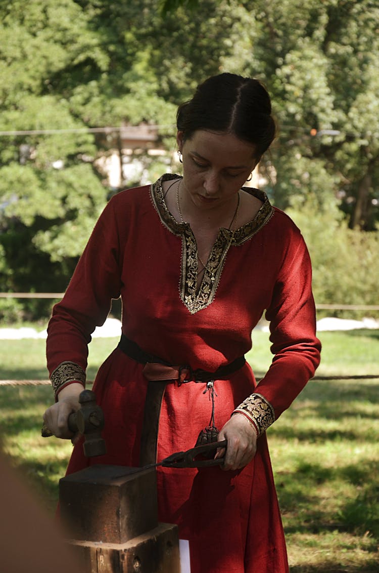 A Woman In Red Medieval Clothing Holding A Hammer And Pliers