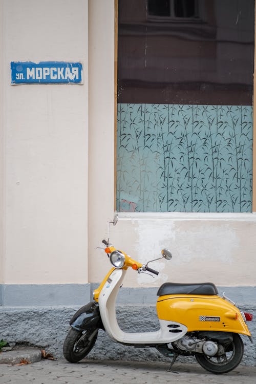 Photo of a Yellow and White Scooter Parked Near a Wall