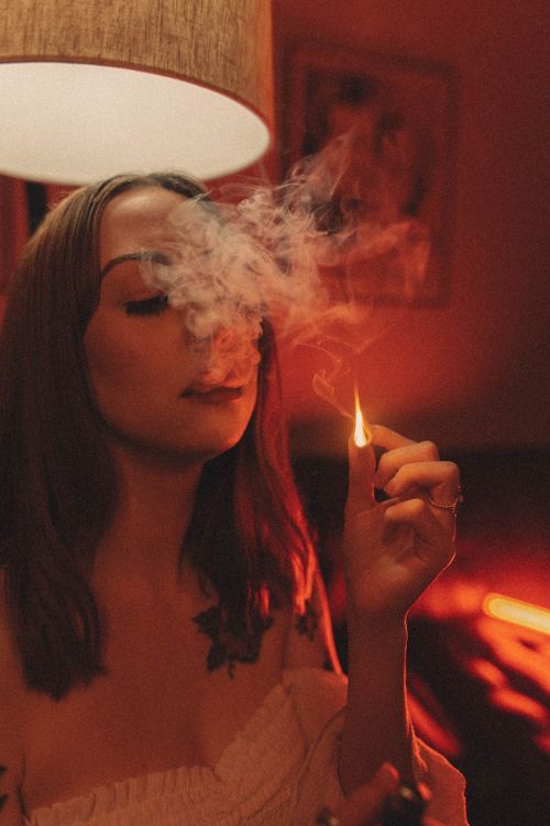 Free Artistic photo of a tattooed woman smoking indoors with warm moody lighting. Stock Photo