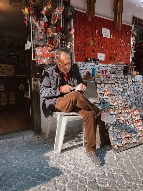 Free A senior man sells souvenirs at a market stall in Eskişehir, Turkey. Sunlit scene captures the vibrant street life. Stock Photo