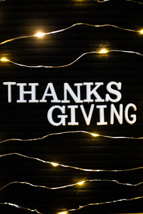 Free Thanksgiving text with glowing string lights on a dark background, creating a festive atmosphere. Stock Photo