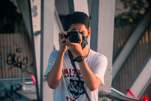 Man in White Shirt and Face Mask Using a Black Camera