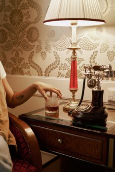 Elegant vintage room with lamp, antique phone, and person holding a glass.